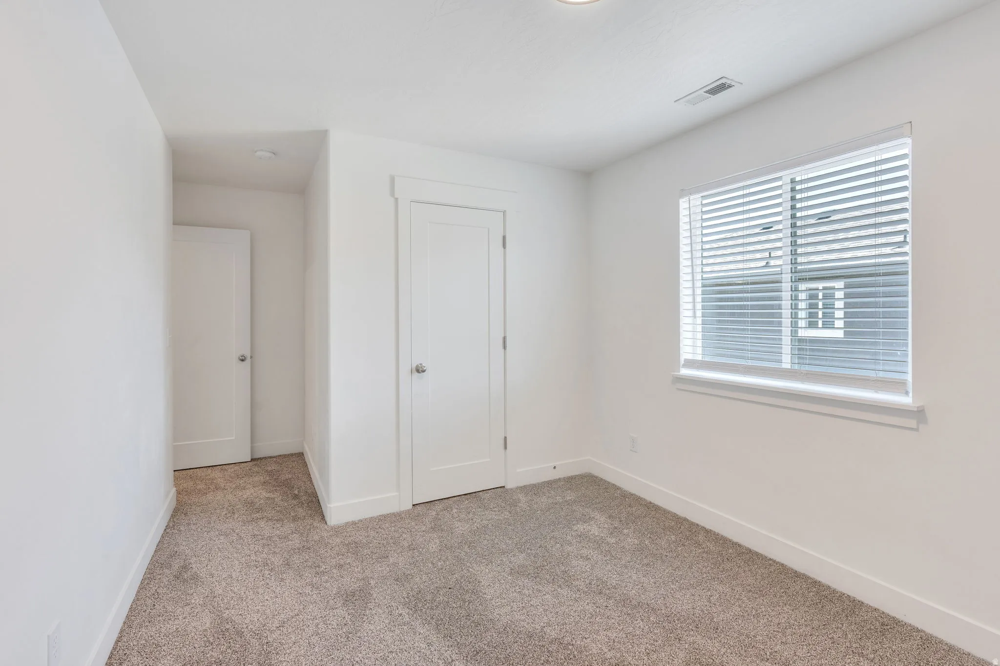 Bedroom featuring neutral carpet, white walls, and a single window with horizontal blinds