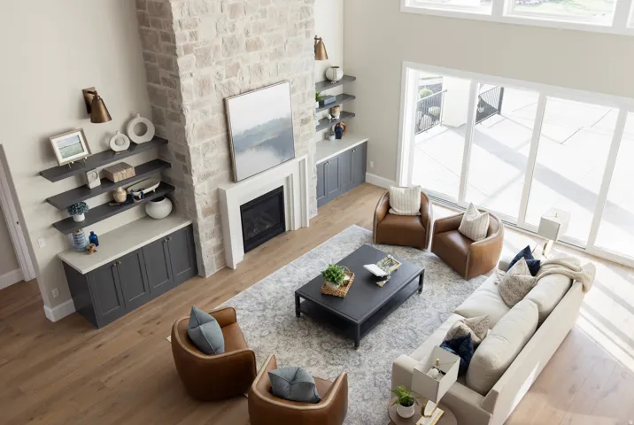Spacious living area featuring a stone-clad fireplace with a white mantel, built-in cabinetry with light countertops, dark floating shelves, and wood-finish flooring