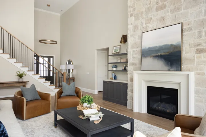 Two-story living area featuring a stone-clad fireplace with a white mantel, built-in shelving, wood-finish flooring, a staircase with black metal balusters, and a dark-paneled entry door