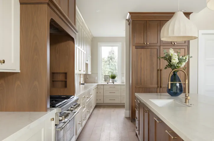 Gourmet kitchen featuring a wood-panel range hood, stainless steel gas range, integrated paneled refrigeration, a large central island with an undermount sink, and wood-finish flooring