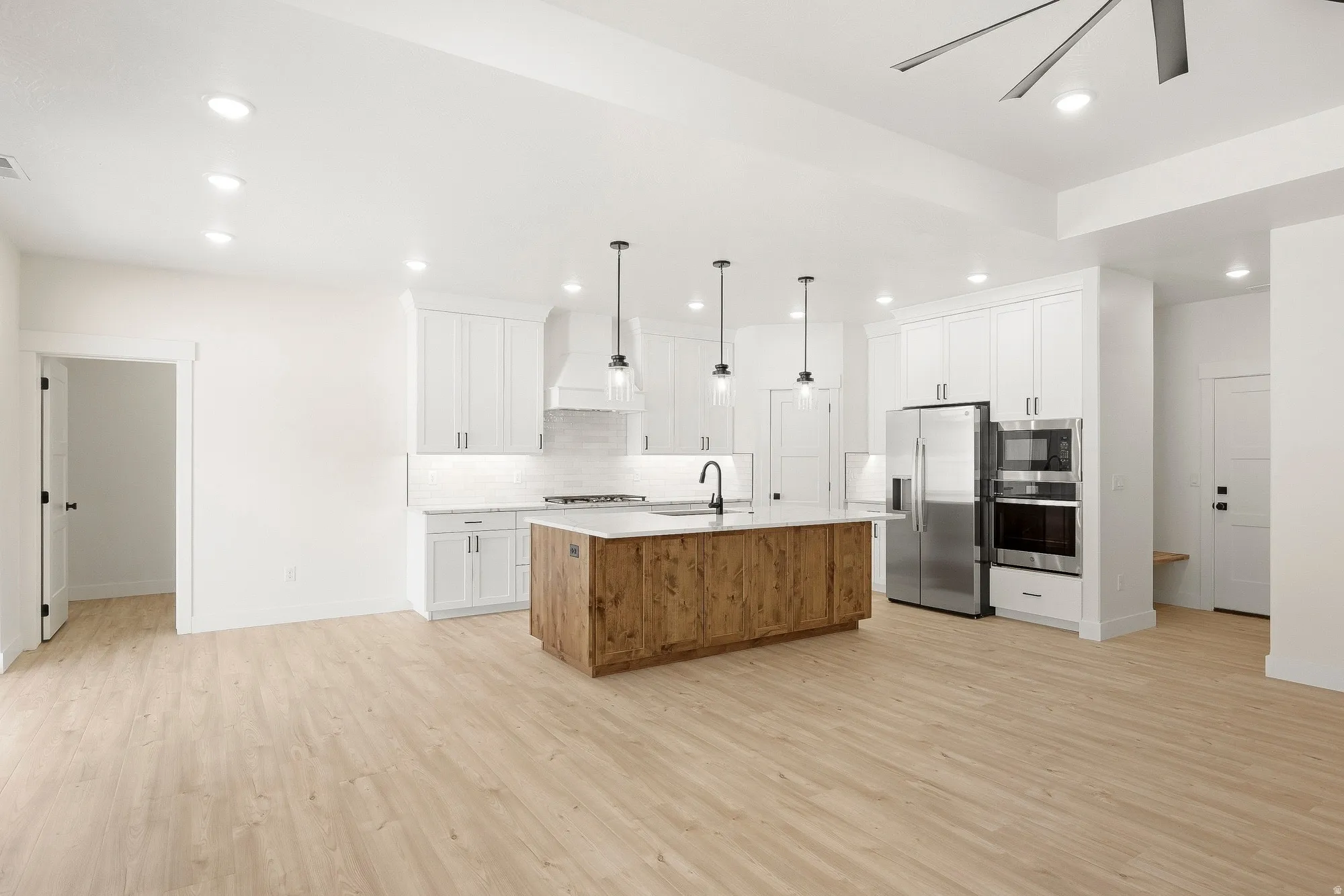 Modern kitchen featuring a wood-finish island with a light-toned countertop, white cabinetry with dark hardware, stainless steel appliances, and wood-finish flooring