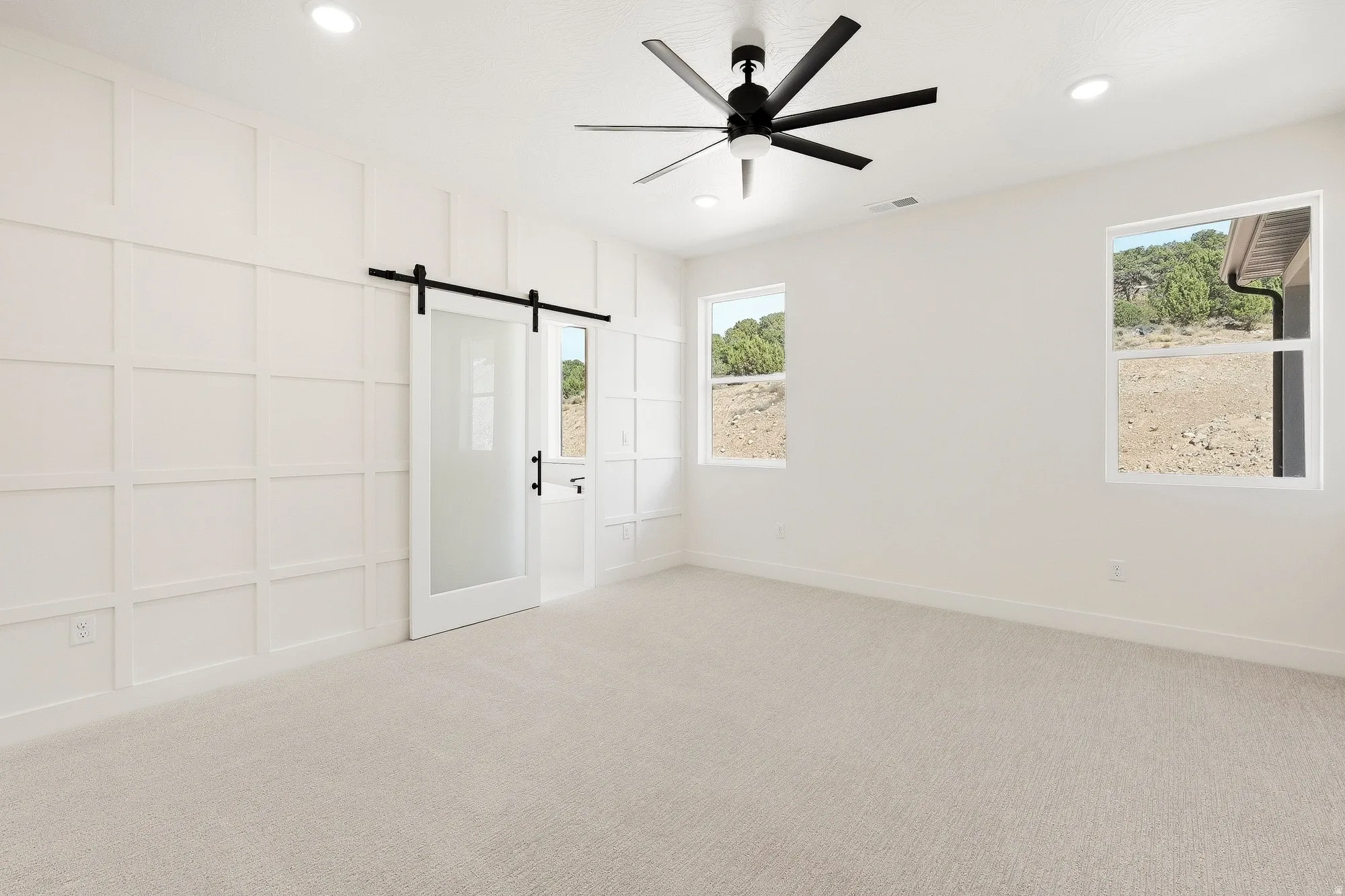 White paneled wall accent, frosted glass barn door, recessed lighting, modern ceiling fan, and carpeted flooring