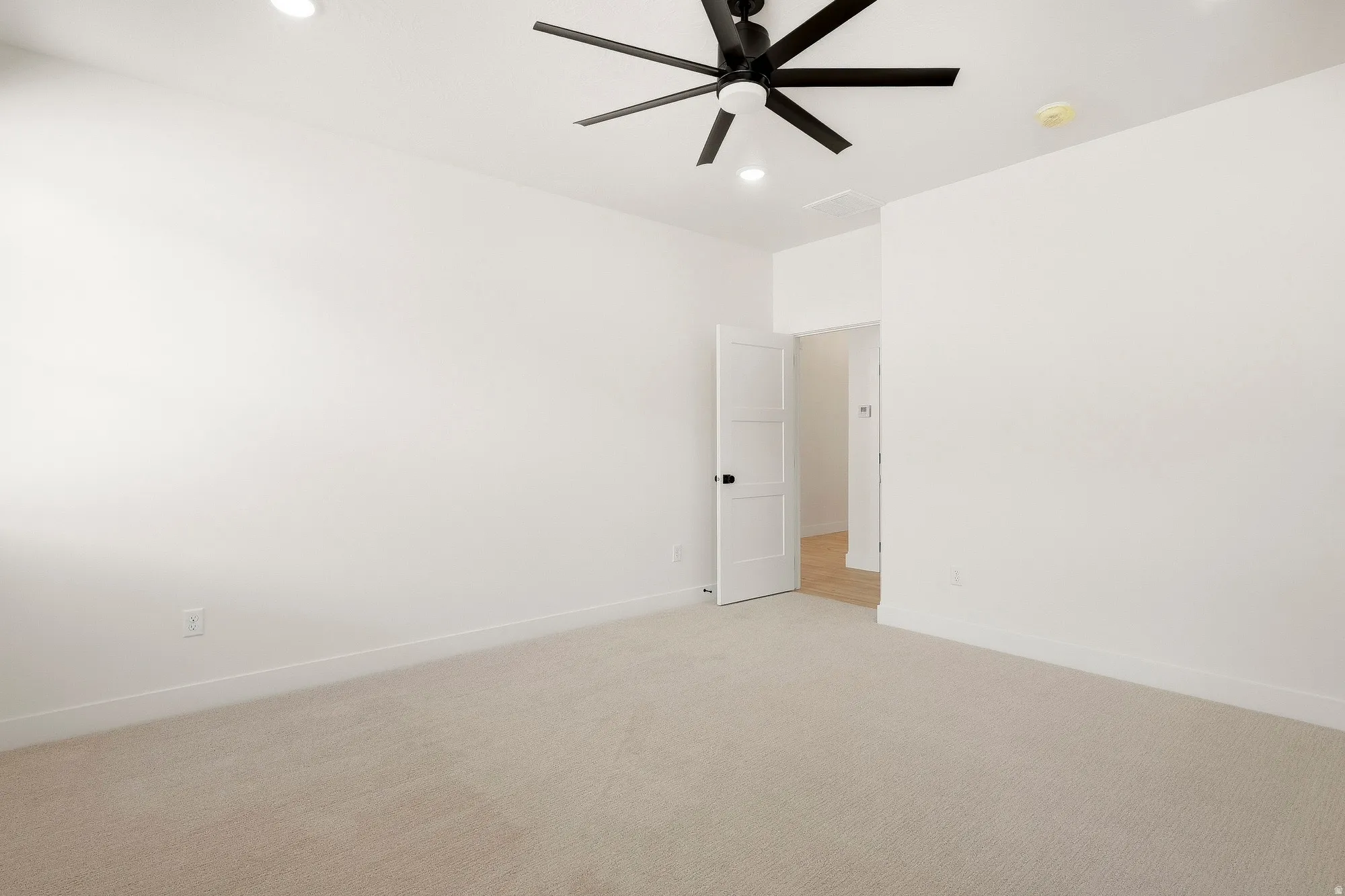 Recessed lighting, ceiling fan, white paneled door, light-toned carpeting, and wood-finish flooring visible beyond