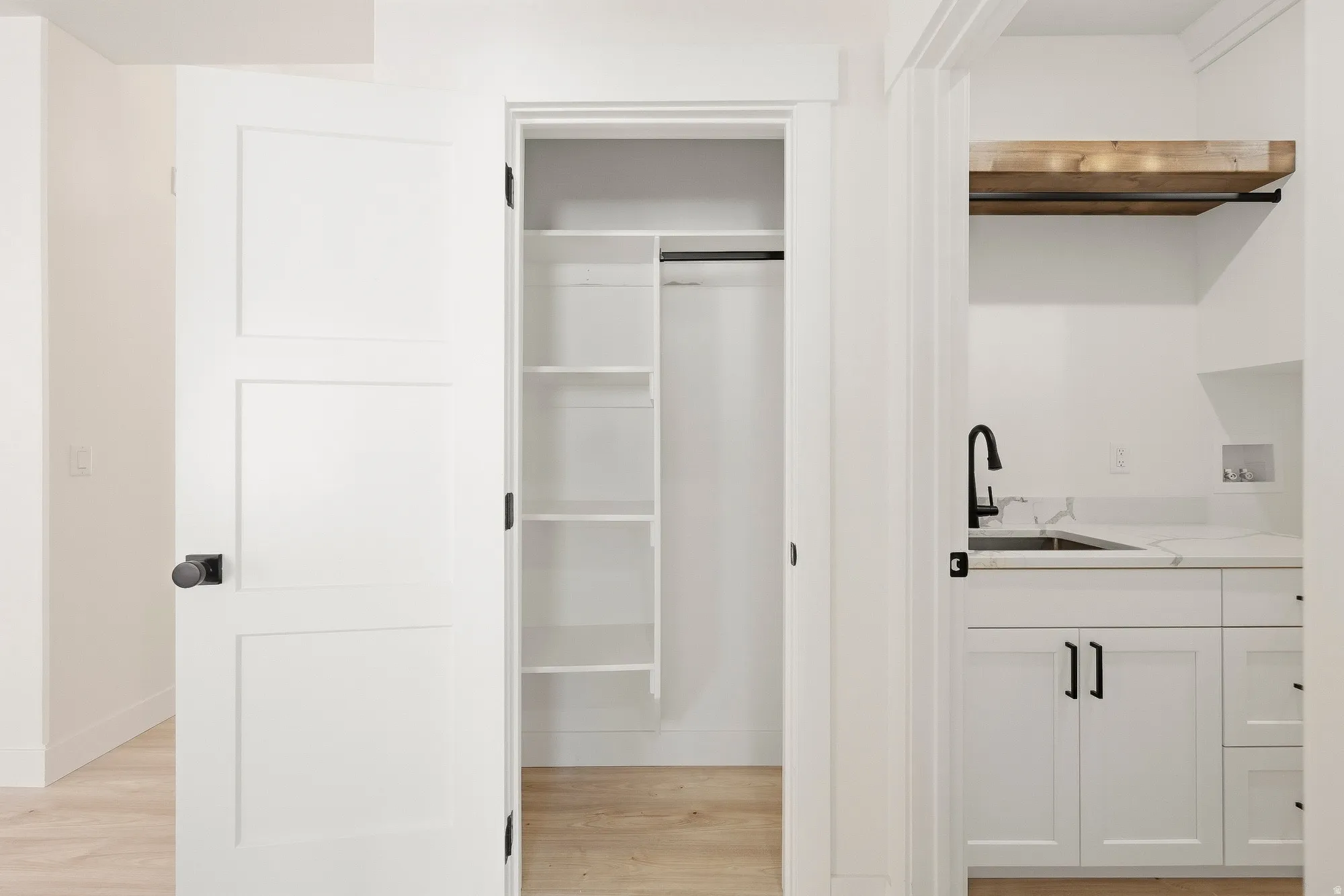 Laundry area featuring white cabinetry, a sink with a matte black faucet, and a light wood-finish shelf