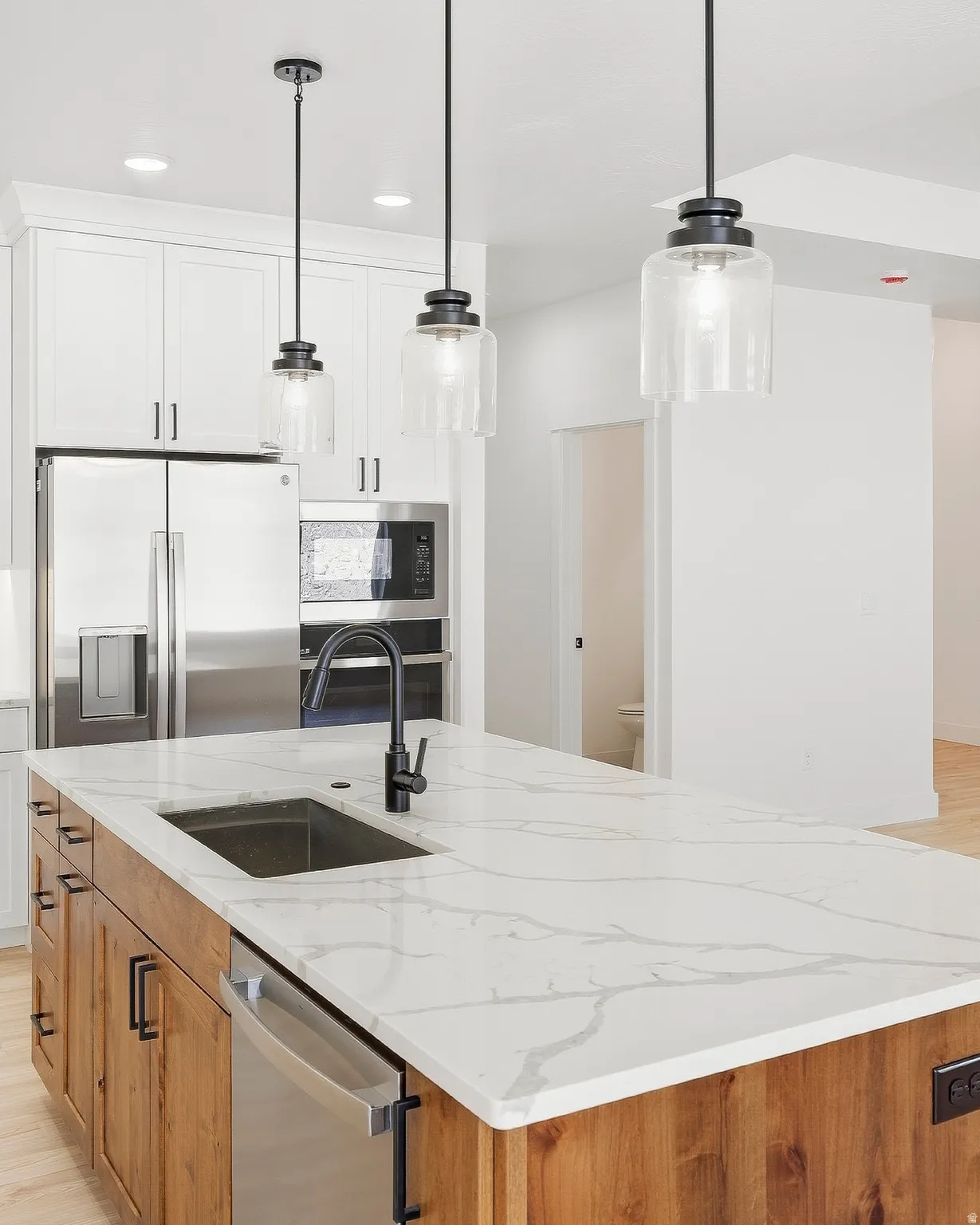 Kitchen island with a white countertop and integrated sink, under-cabinet lighting, stainless steel appliances, and wood-finish flooring
