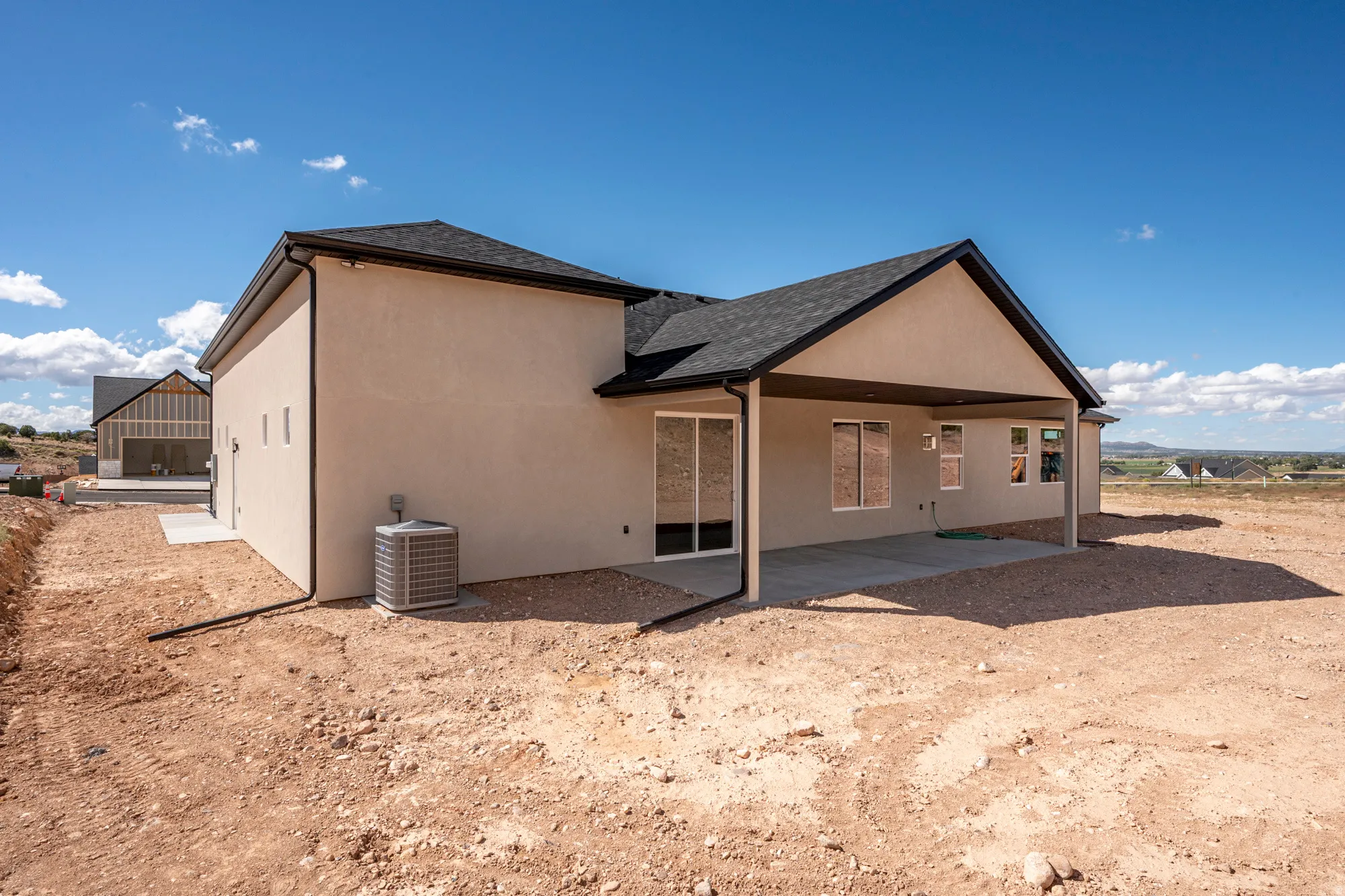 Stucco exterior with a covered patio, dark roof shingles, and a visible HVAC unit