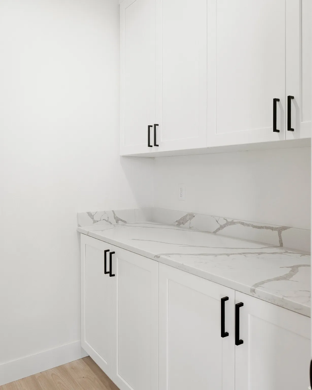 White shaker-style cabinetry with matte black hardware, stone-finish countertops, and wood-finish flooring