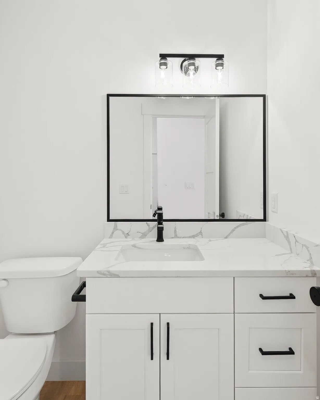White vanity with shaker-style cabinetry, matte black hardware, integrated rectangular sink, and stone-look countertop