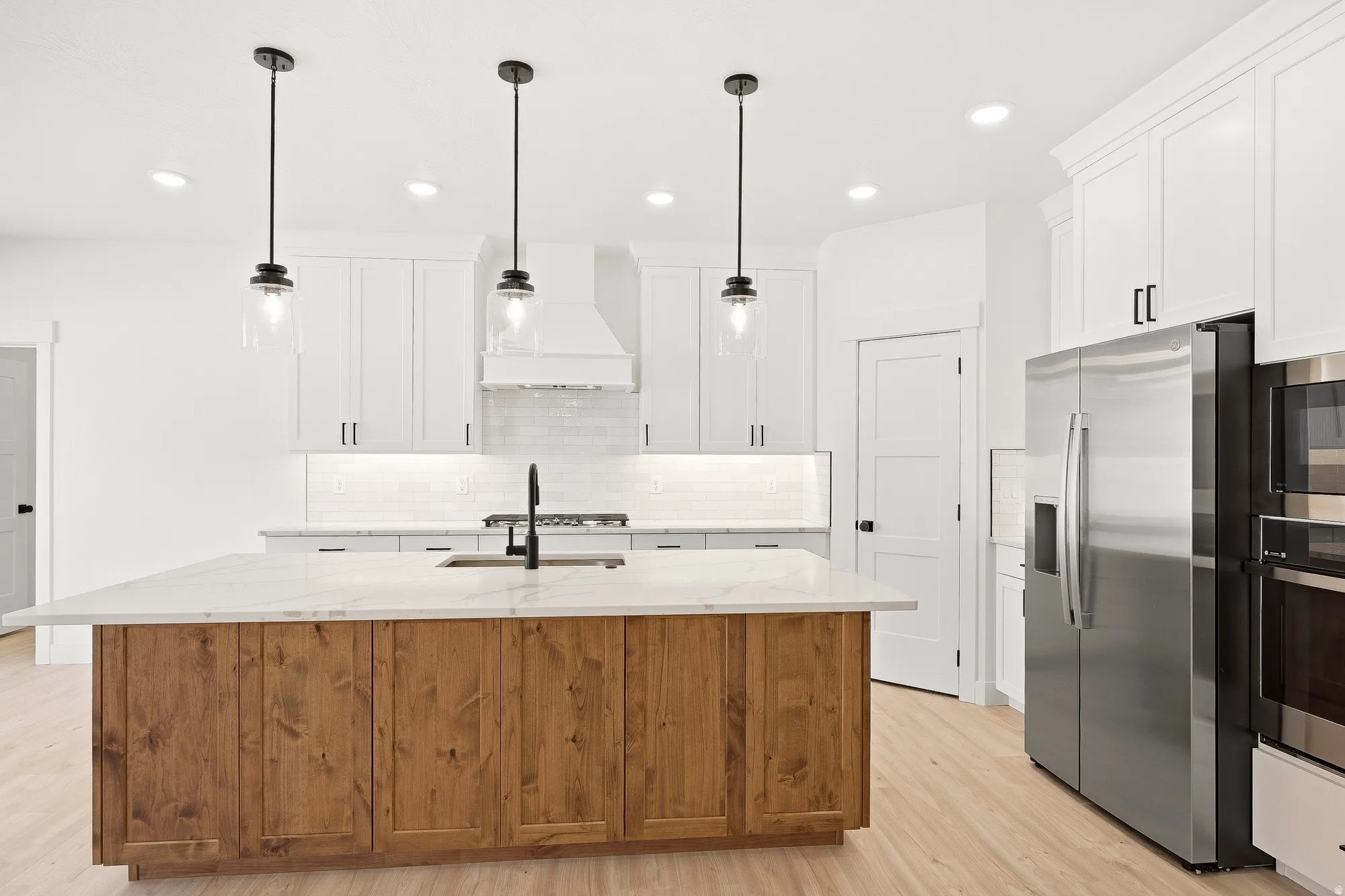 Kitchen featuring a wood-finish island with a stone countertop, stainless steel appliances, white cabinetry, and pendant lighting