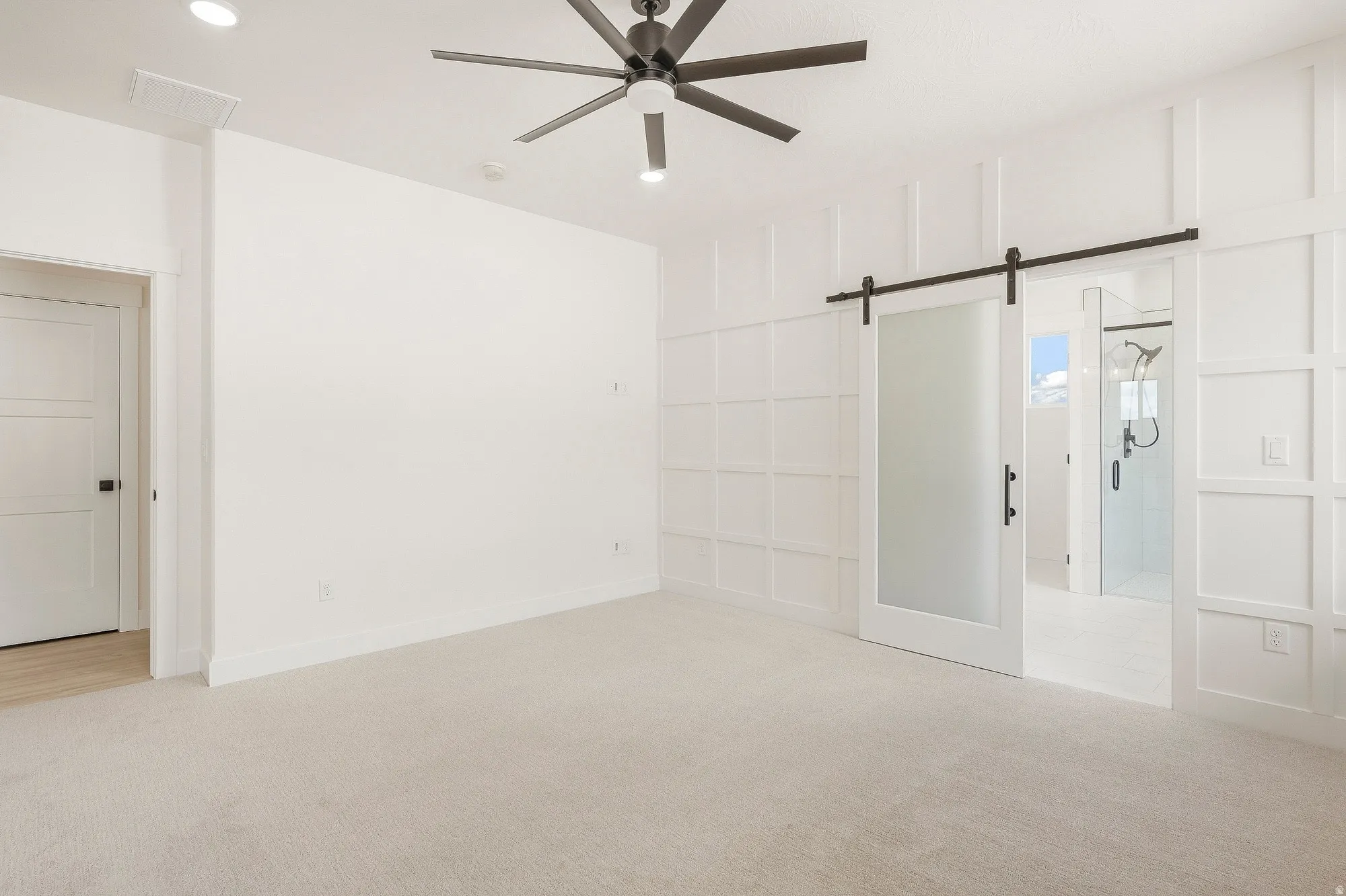White paneled accent wall, barn door entry with frosted glass panel, recessed lighting, ceiling fan, and carpeted flooring