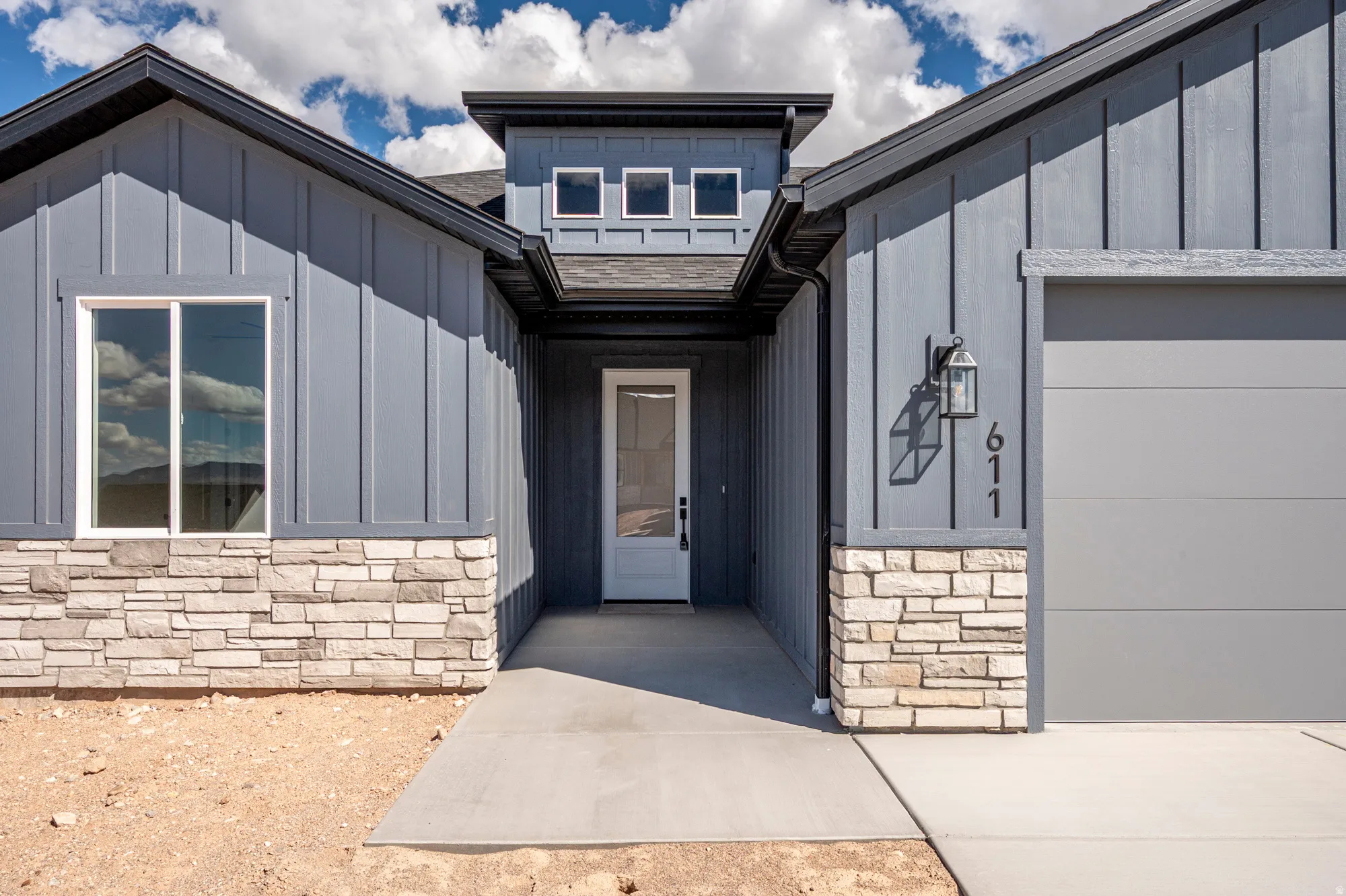 Modern exterior featuring vertical board and batten siding, stacked stone accents, a gray garage door, and a white entry door