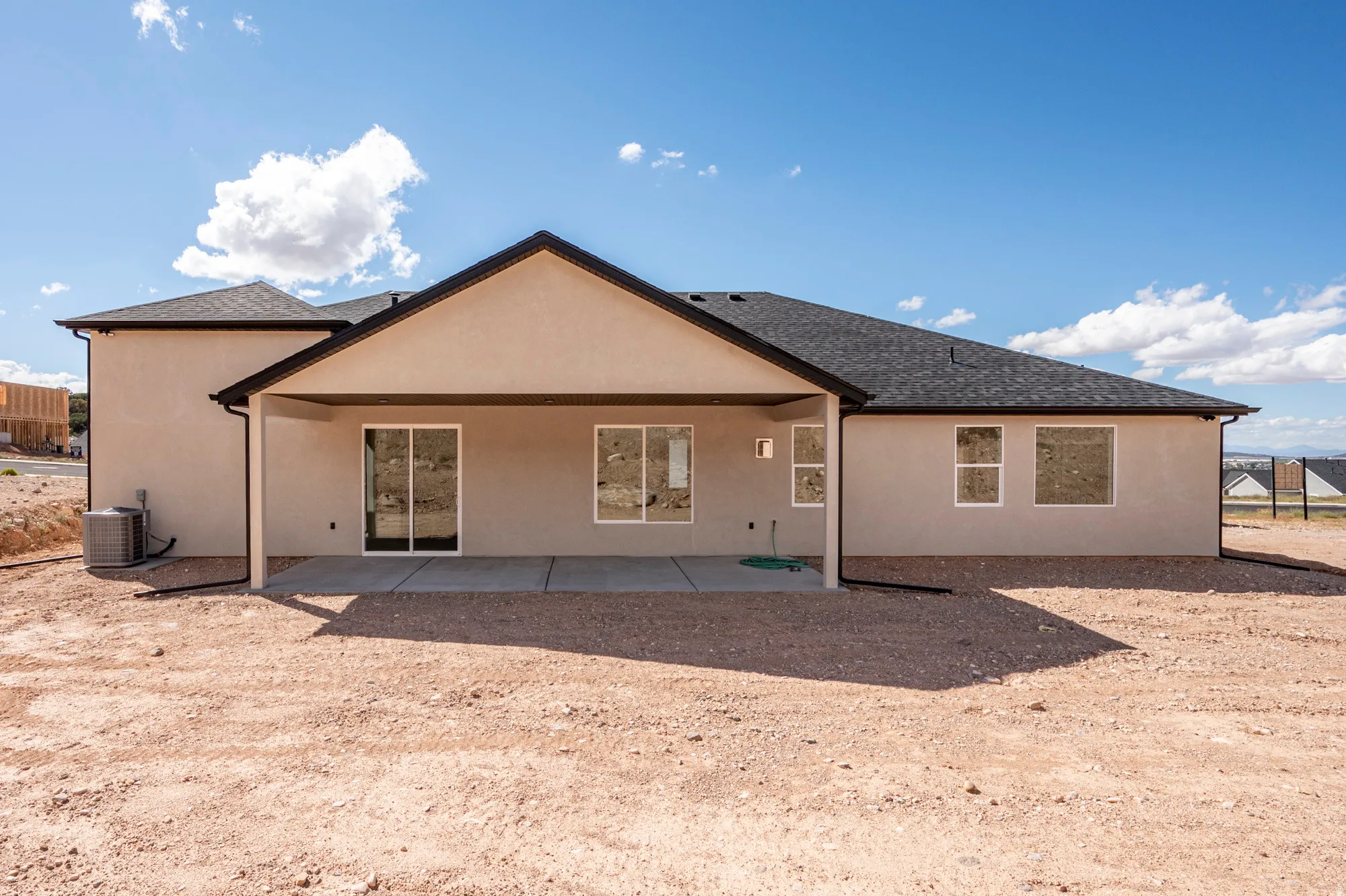 Stucco exterior with a covered patio, an exterior air conditioning unit, and a shingle roof