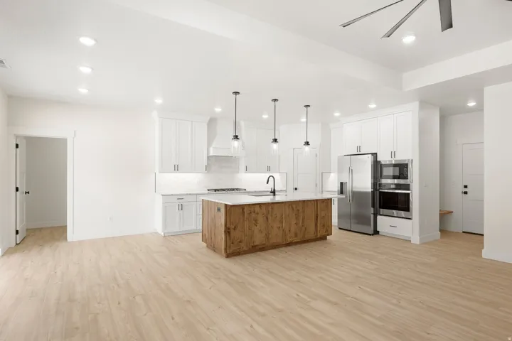 Modern kitchen featuring a wood-finish island with a light-toned countertop, white cabinetry with dark hardware, stainless steel appliances, and wood-finish flooring