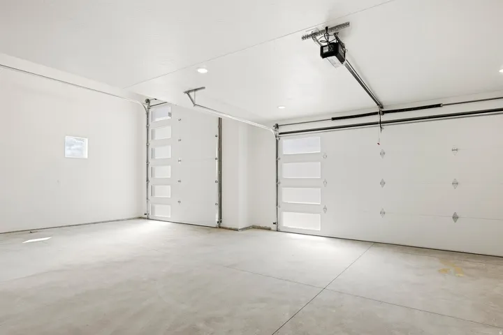Two overhead garage doors with integrated window panels, concrete flooring, and recessed lighting