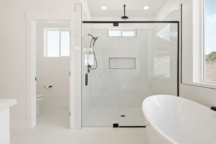 Walk-in shower with black-framed glass enclosure, freestanding soaking tub, recessed shower niche with mosaic tile, overhead rainfall shower, and a secondary handheld showerhead
