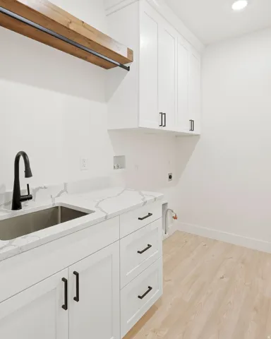 White cabinetry with matte black hardware, quartz-finish countertop, undermount stainless steel sink, black gooseneck faucet, and wood-finish flooring