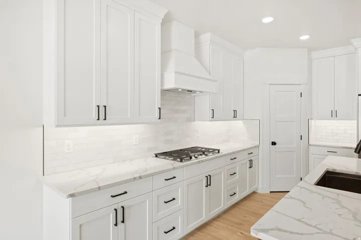 White shaker cabinetry, stone countertops with integrated sink, subway tile backsplash, stainless steel gas cooktop, and wood-finish flooring