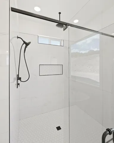 Glass-enclosed shower with a rain shower head, handheld shower, recessed niche with hexagonal tile, and hexagonal floor tiling