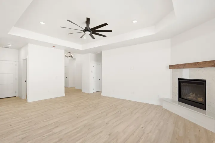 Recessed lighting, ceiling fan, fireplace with a wood mantel, light wood-finish flooring, and tray ceiling