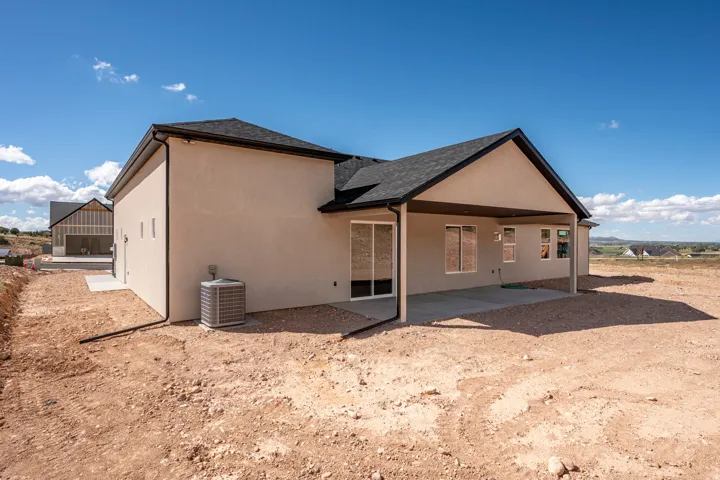 Stucco exterior with a covered patio, dark roof shingles, and a visible HVAC unit