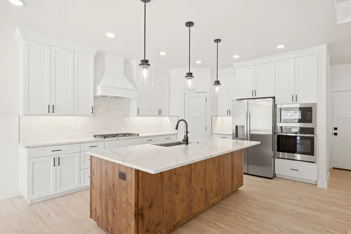Gourmet kitchen featuring white shaker cabinetry, stainless steel appliances, a wood-finish island with a waterfall countertop, and wood-finish flooring