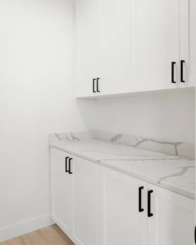 White shaker-style cabinetry with matte black hardware, stone-finish countertops, and wood-finish flooring