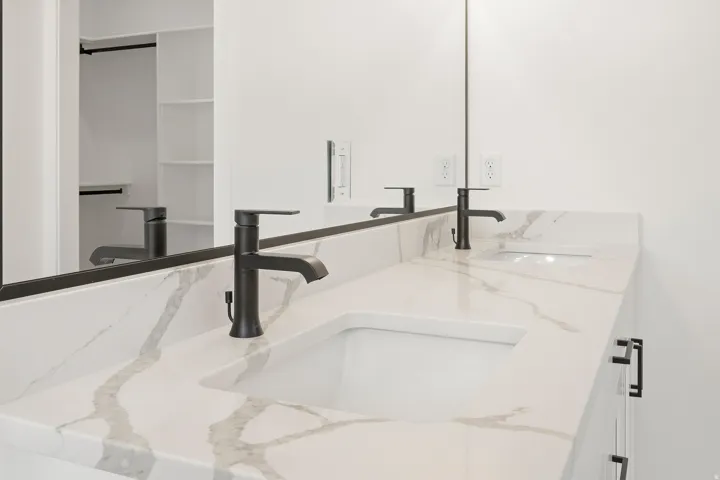 White vanity with dual integrated sinks, matte black faucets, and a stone-finish countertop