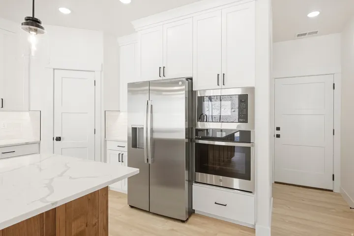 White cabinetry, stainless steel appliances, light wood-finish flooring, white countertops, and a built-in oven