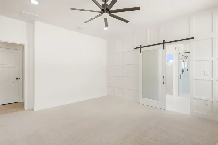 White paneled accent wall, barn door entry with frosted glass panel, recessed lighting, ceiling fan, and carpeted flooring