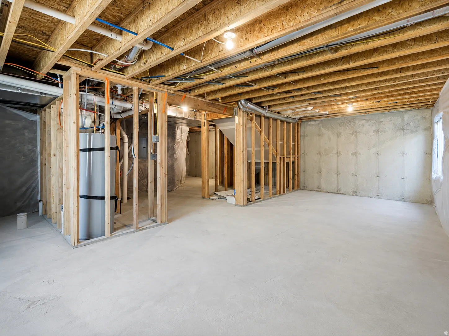 Unfinished basement featuring concrete flooring, exposed wood joists, framed interior walls, visible plumbing, and electrical wiring