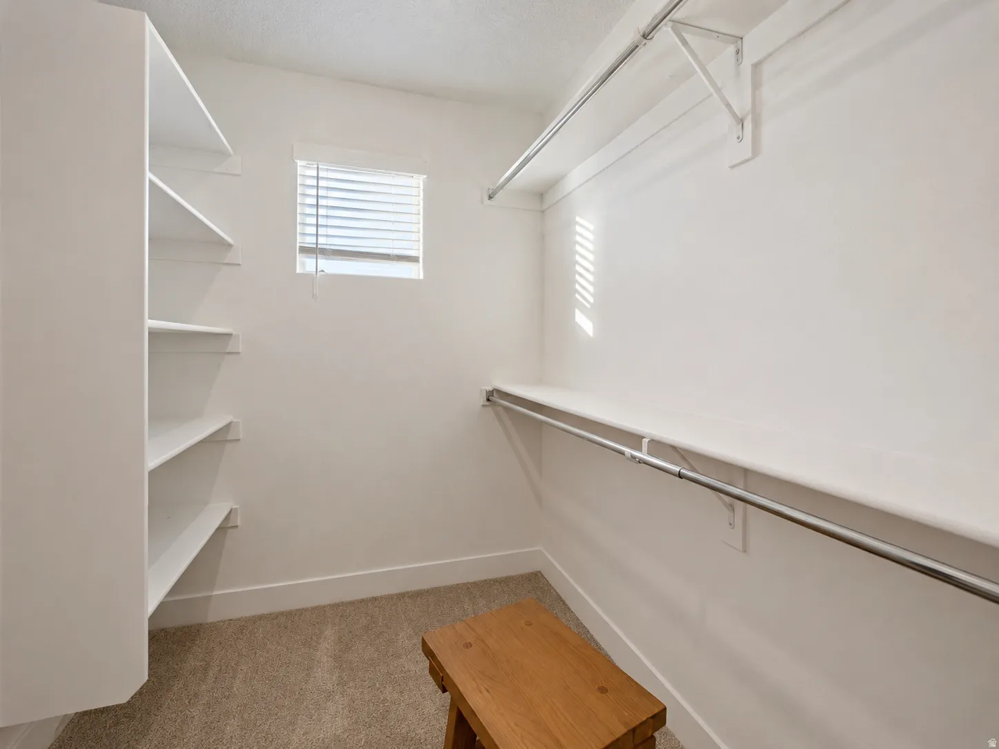 Spacious walk-in closet featuring built-in shelving, carpet flooring, a window with blinds, and multiple clothing rods