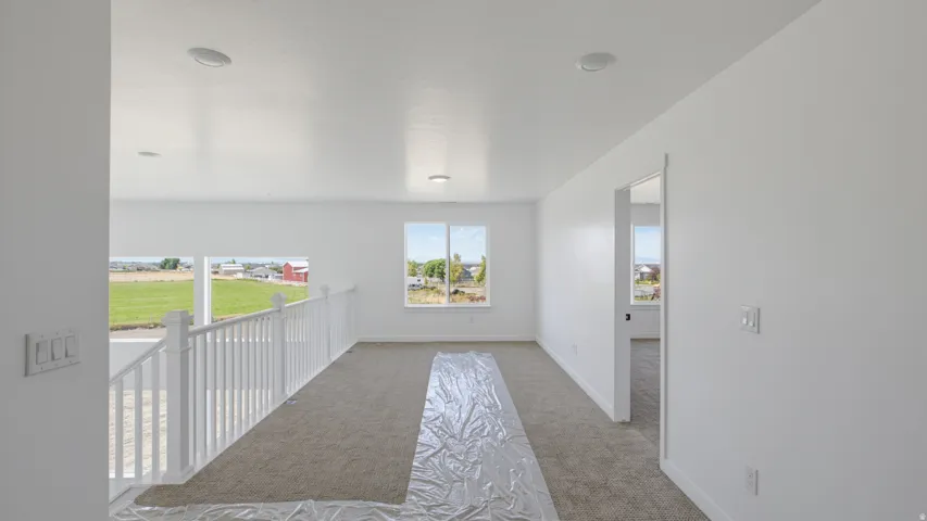 Upper-level area featuring neutral carpet flooring, white walls, multiple windows, recessed lighting, and a white railing