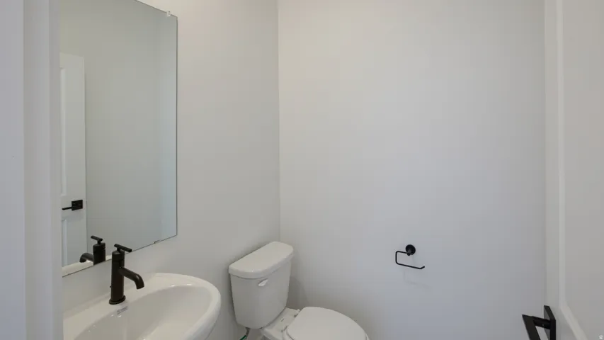 Pedestal sink with a matte black faucet, rectangular wall-mounted mirror, and a white toilet
