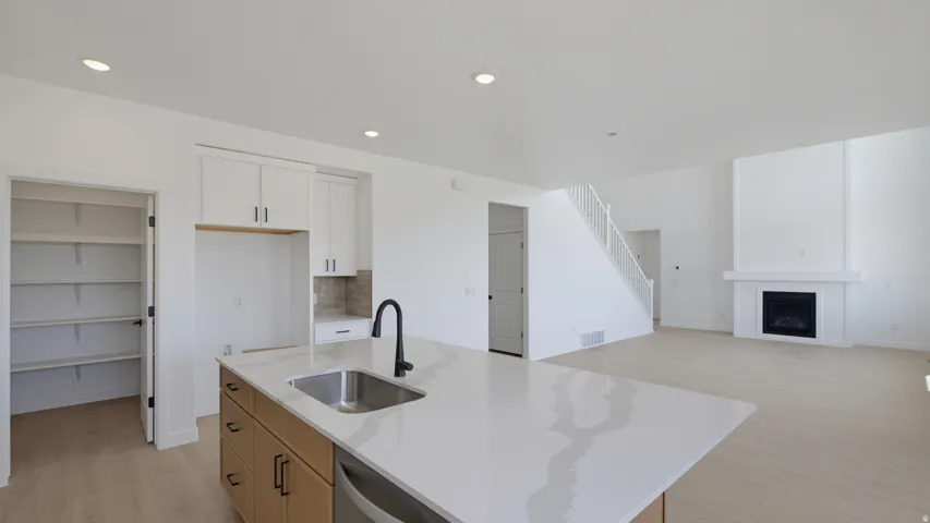Kitchen island with integrated sink, white upper cabinetry, wood-finish lower cabinetry, walk-in pantry, and a living area with a fireplace