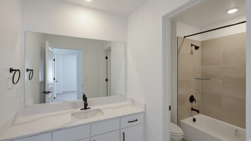 Bathroom featuring a white vanity with an integrated sink, matte black fixtures, a full-width mirror, and a tub-shower combination with light-toned wall tiling