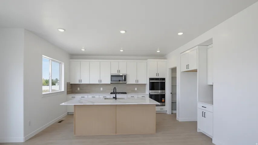 Contemporary kitchen featuring white cabinetry, a large center island with a stone-finish countertop, stainless steel appliances, and wood-finish flooring