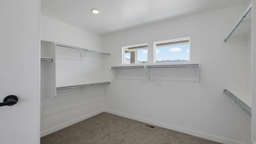 Walk-in closet with integrated shelving, hanging rods, two windows, and recessed lighting