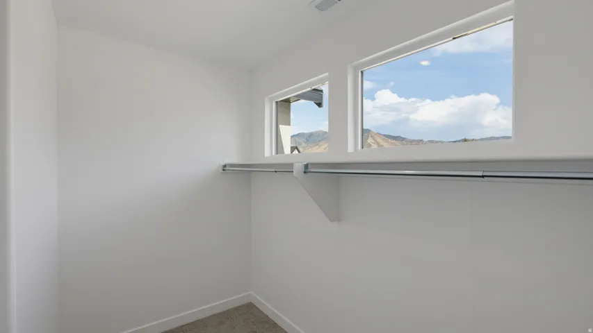 Built-in shelving with a hanging rod, two windows, wall-to-wall carpeting, and white wall finishes