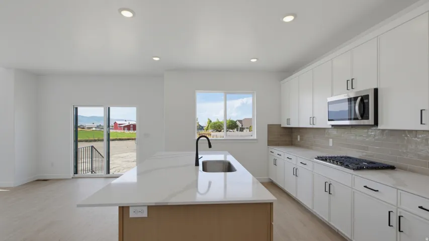 Modern kitchen featuring a central island with an undermount sink, white cabinetry with dark hardware, stainless steel microwave, gas cooktop, and light wood-finish flooring