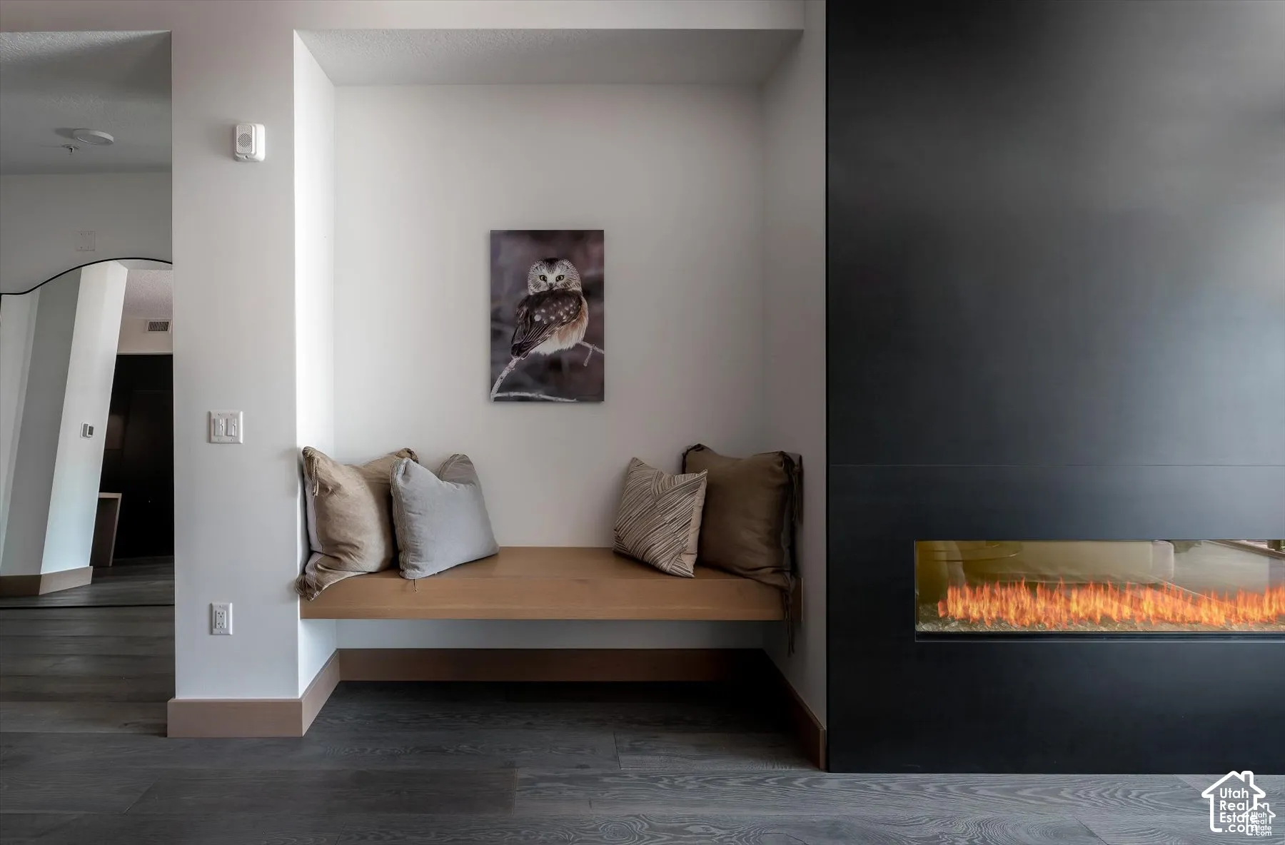 Integrated linear fireplace with a matte black surround, built-in window bench seating, and wood-finish flooring