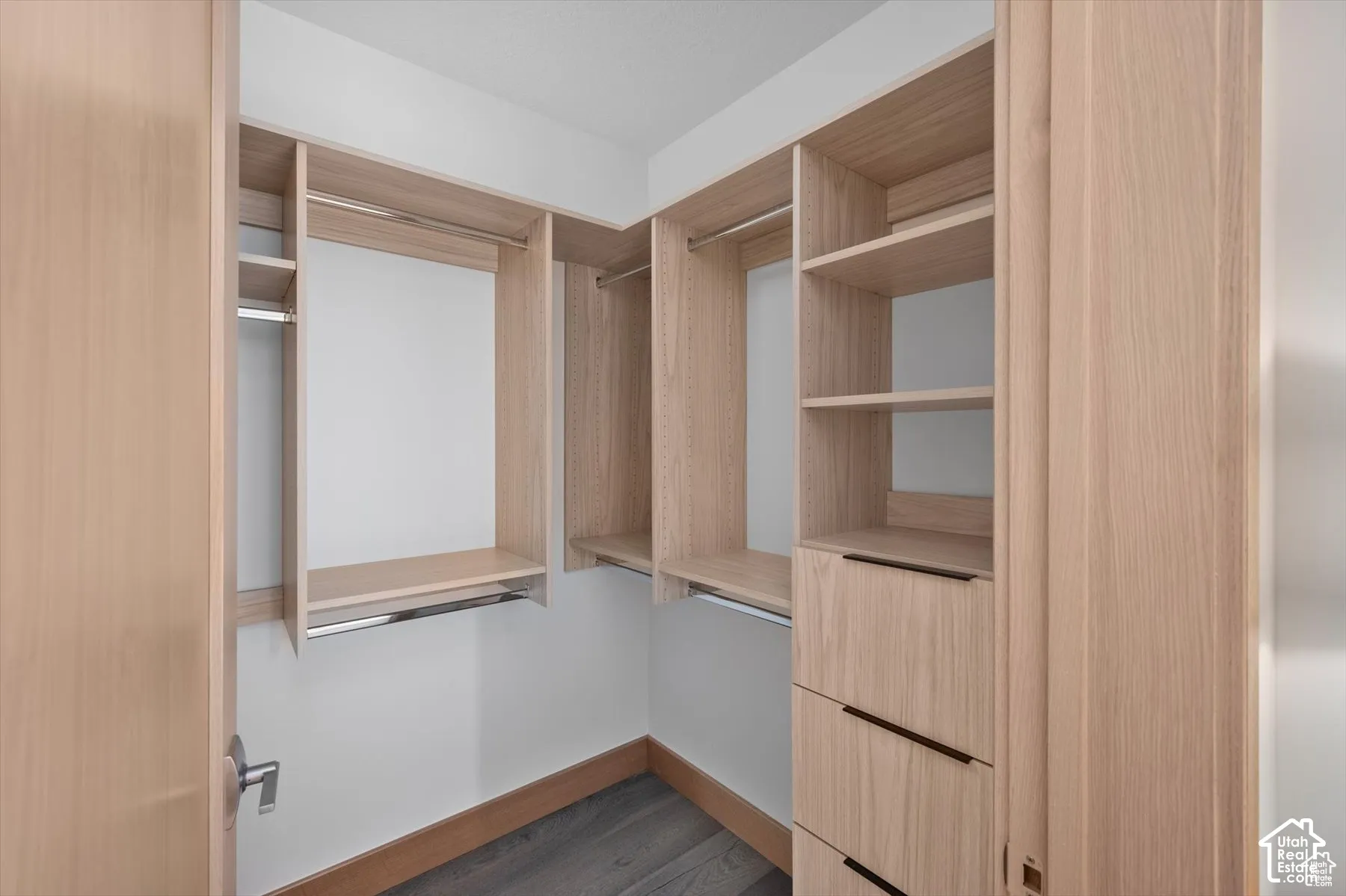 Walk-in closet with custom wood-finish shelving, integrated drawers, chrome hanging rods, and dark wood-finish flooring