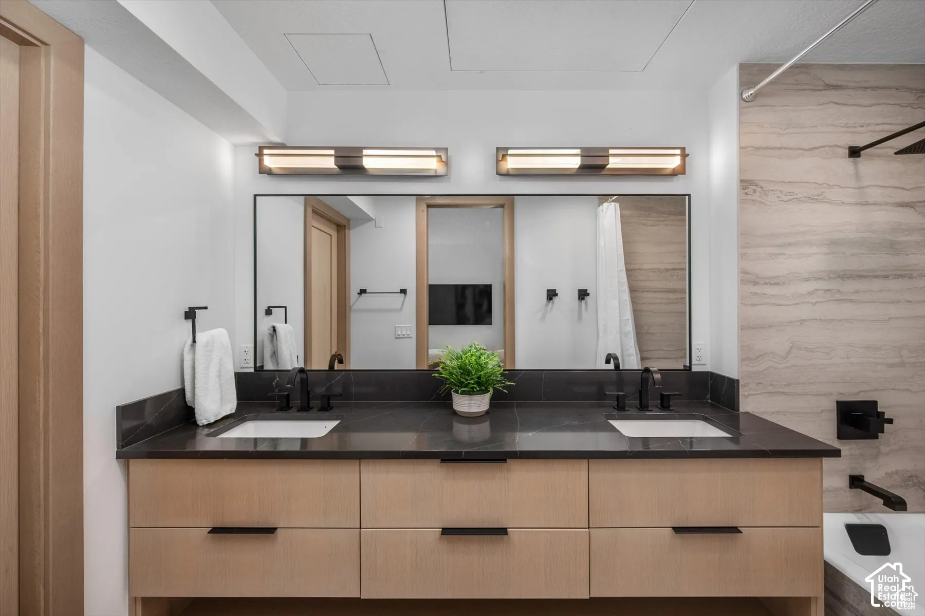 Bathroom featuring a double vanity with light wood-finish cabinetry, a dark stone countertop, and two rectangular undermount sinks
