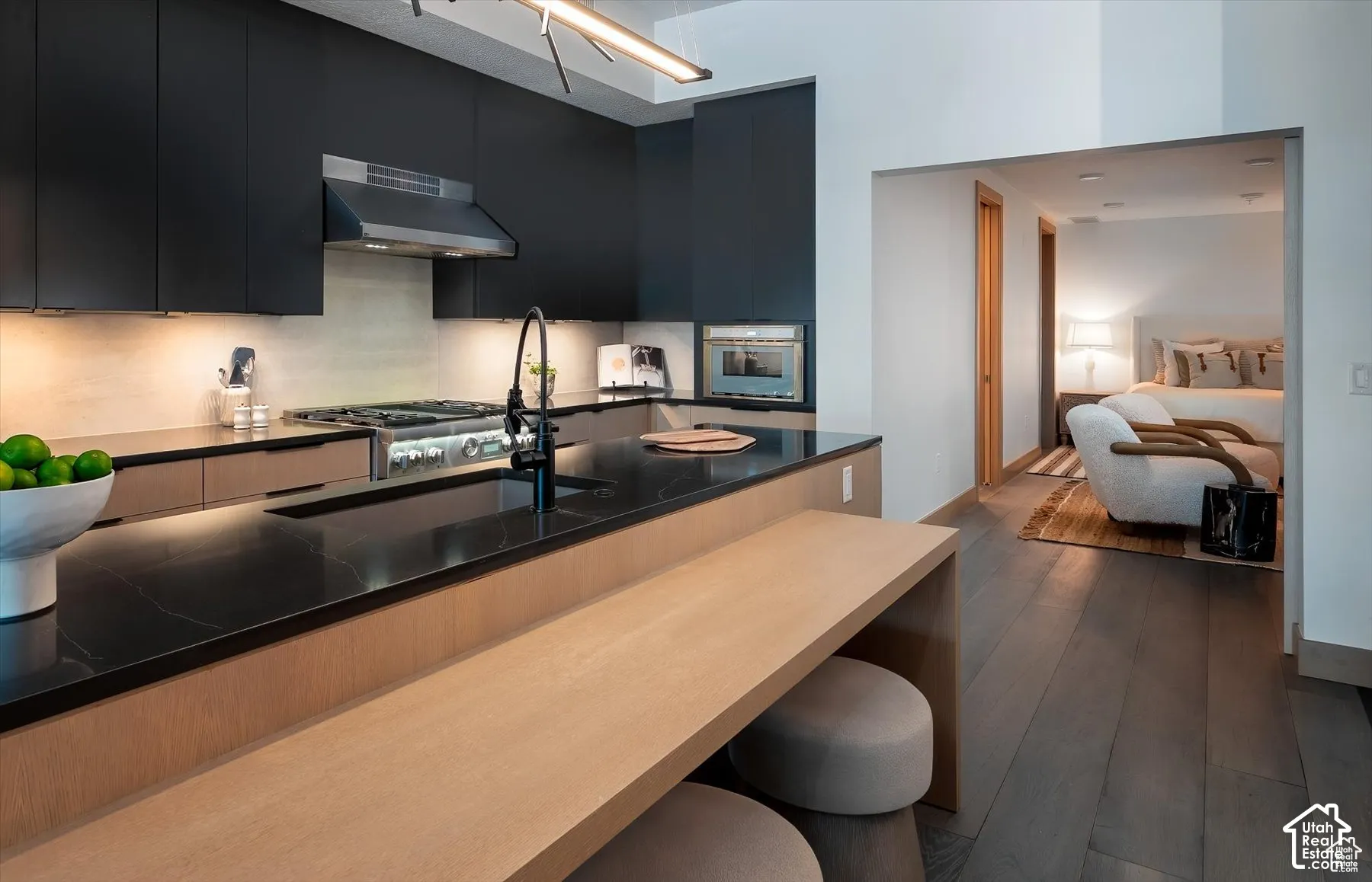 Gourmet kitchen with black cabinetry, dark countertops, a stainless steel range hood, and integrated appliances