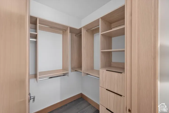 Walk-in closet with custom wood-finish shelving, integrated drawers, chrome hanging rods, and dark wood-finish flooring