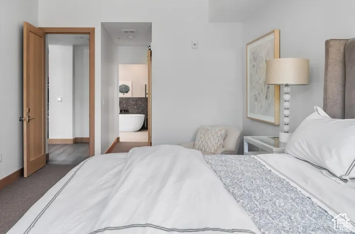 Light-toned bedroom featuring a fabric upholstered headboard, a white nightstand with a mirrored top, and an adjacent wood-paneled doorway