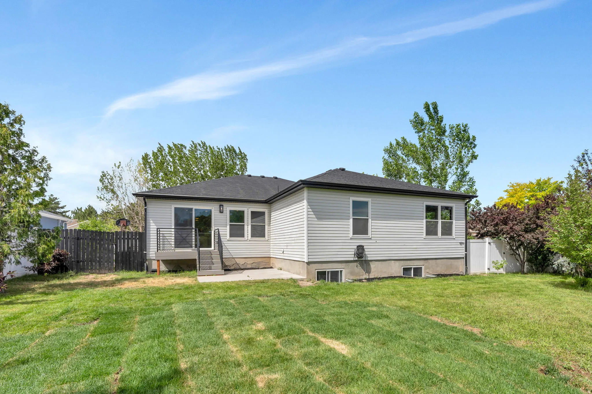 Expansive green lawn surrounds the property, featuring a concrete patio and a raised deck with metal railings