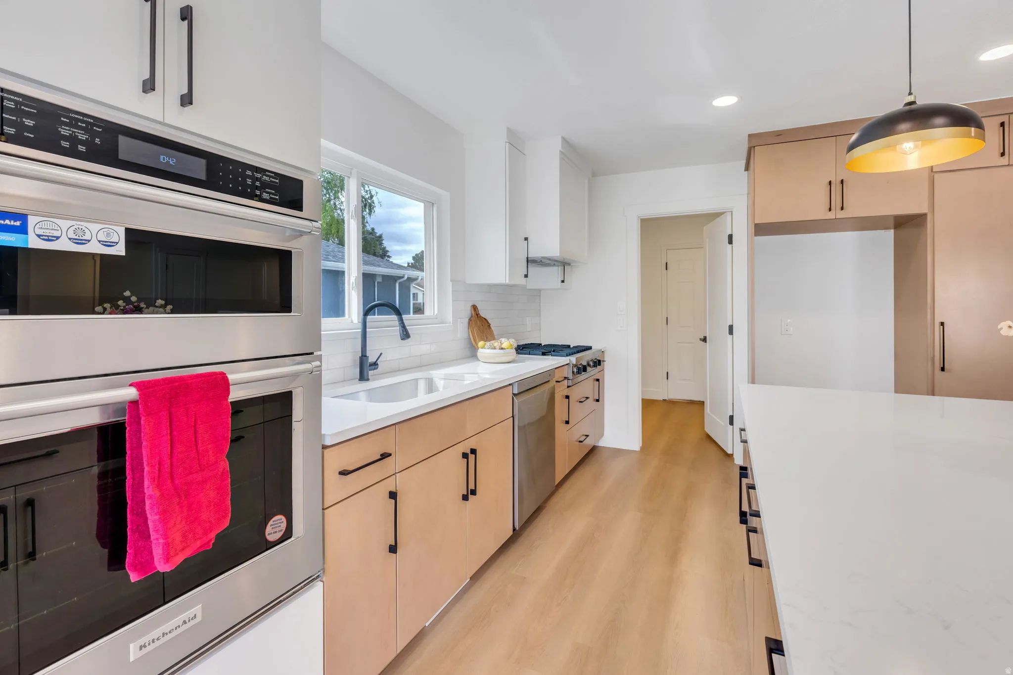Modern kitchen featuring light wood-finish flooring, light-toned cabinetry, and stainless steel appliances