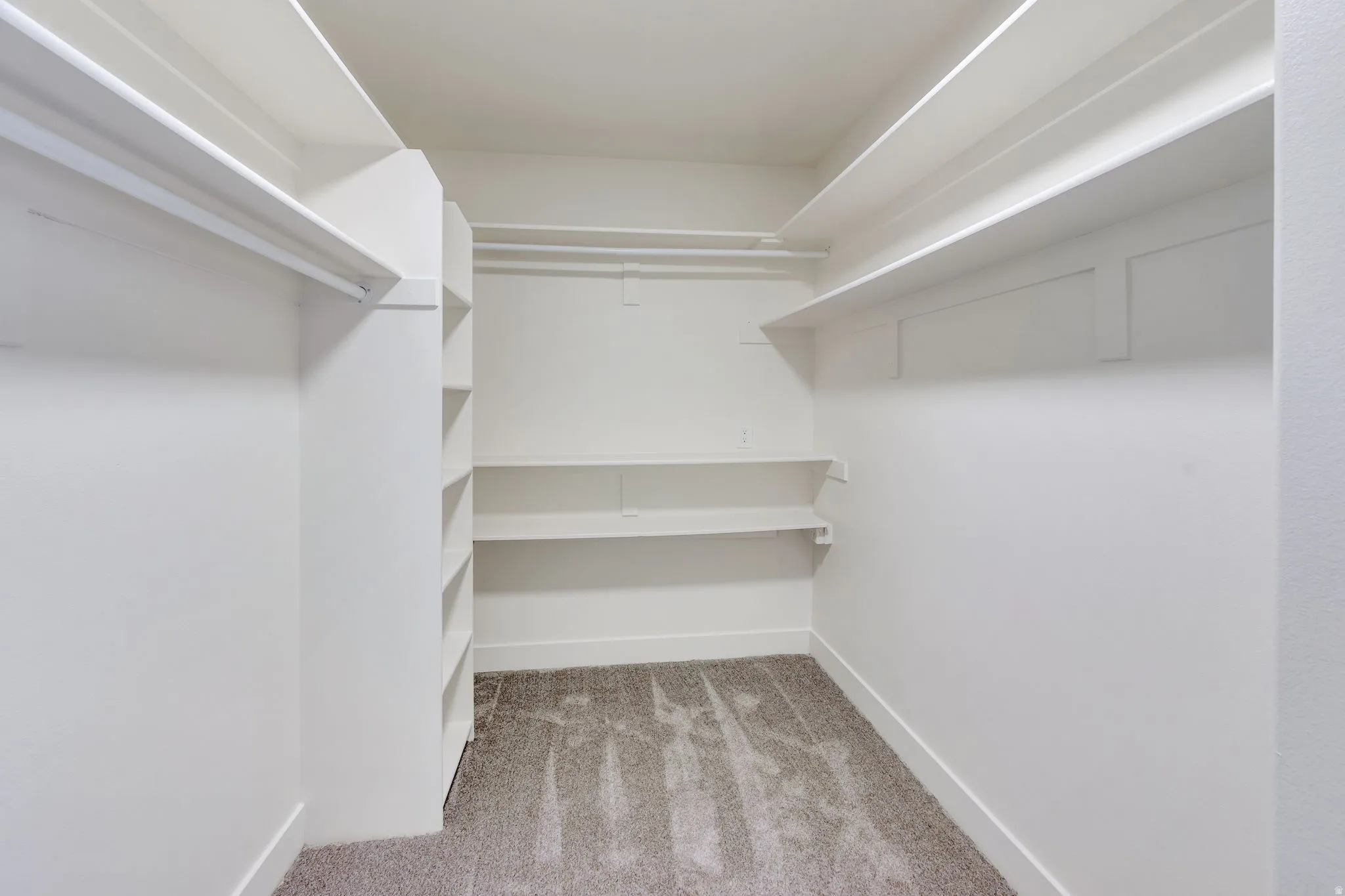 Walk-in closet featuring built-in shelving, multiple hanging rods, and neutral-toned carpeting