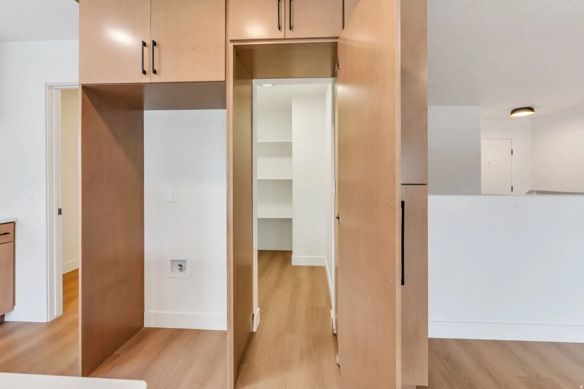 Kitchen pantry with built-in shelving, wood-finish flooring, light wood cabinetry, and contrasting black hardware