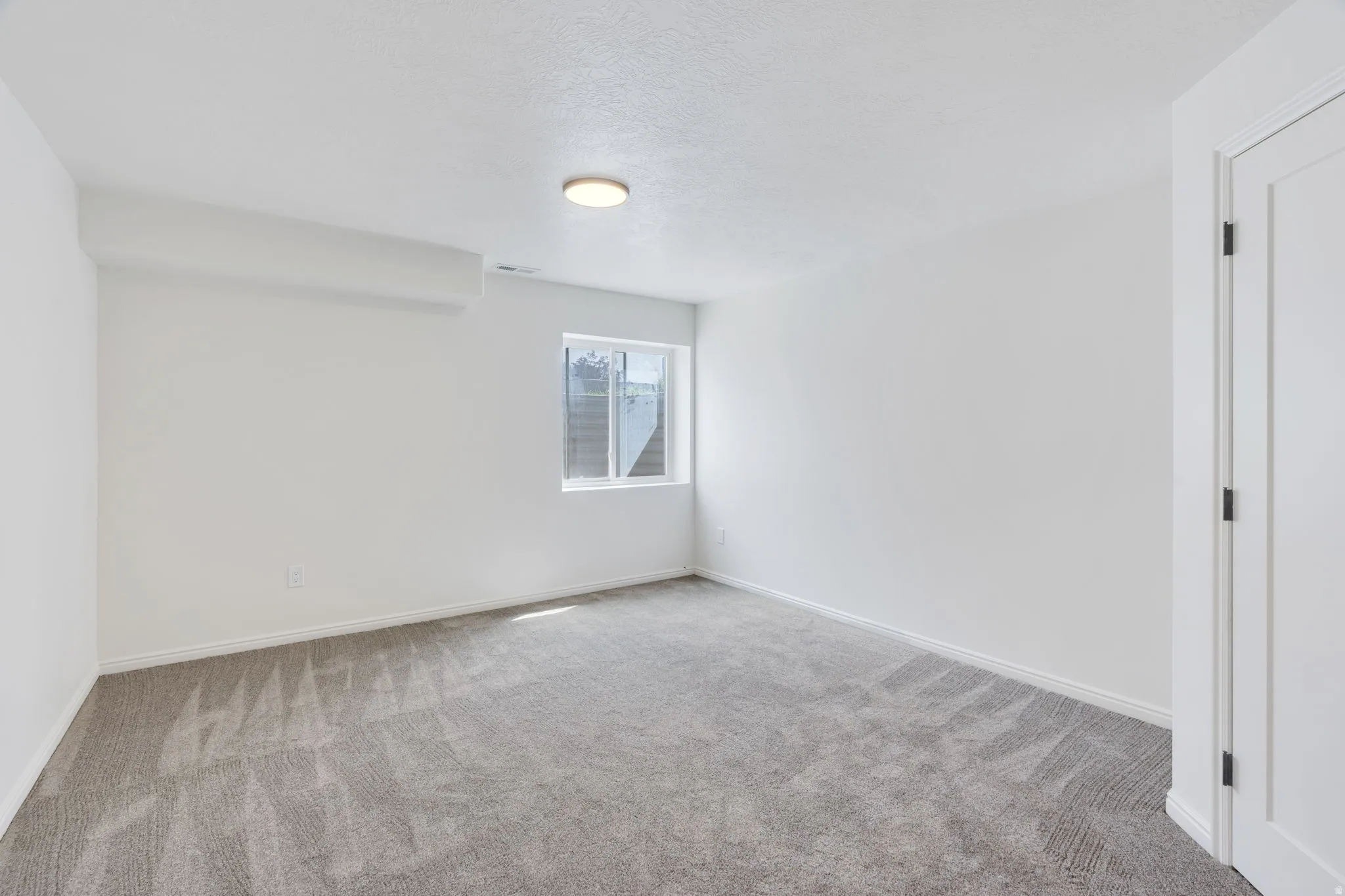Carpeted interior room featuring white walls, a single window, and a flush mount ceiling light